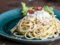 Porcja spaghetti carbonara posypana startym serem, podana na turkusowym talerzu z sałatką.