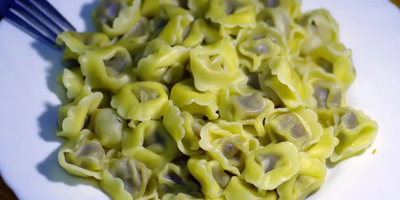Talerz pełen ugotowanego tortellini z widelcem po lewej stronie.