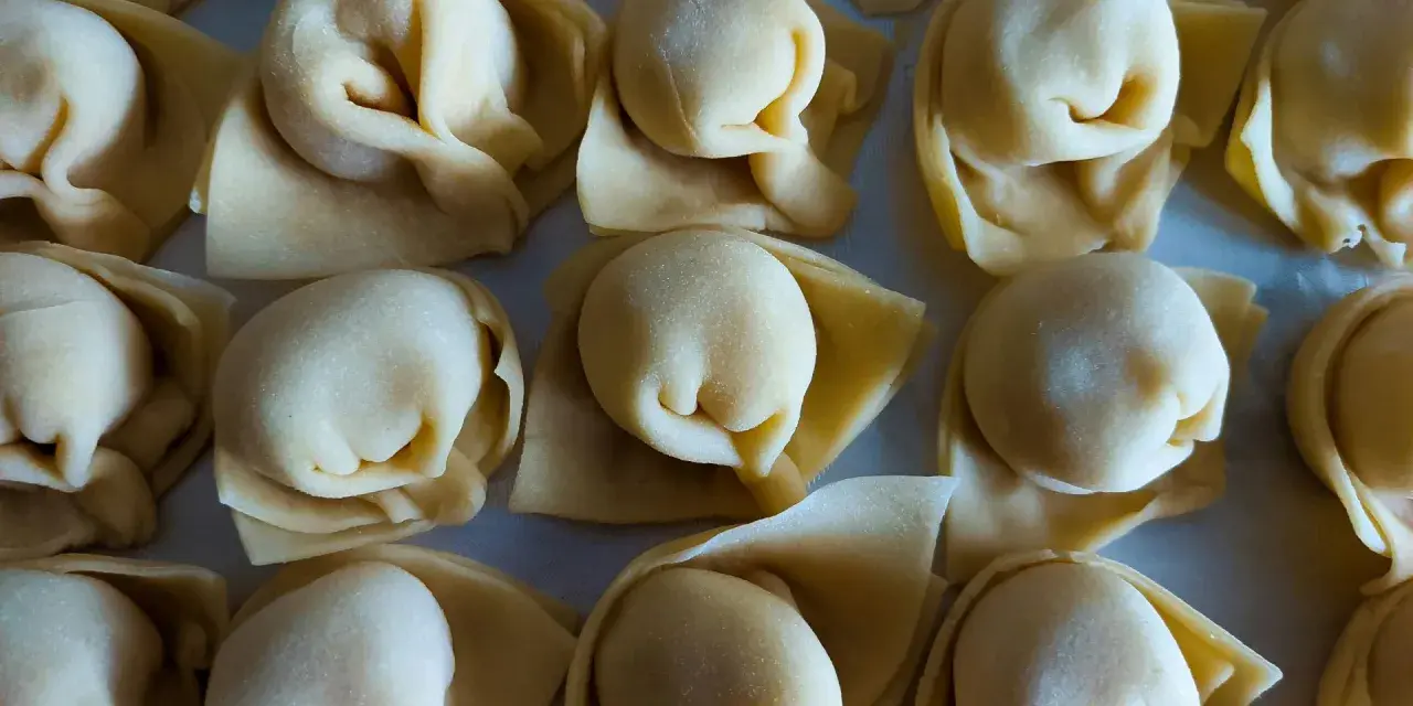 Surowe tortellini ułożone rzędami na jasnym tle.