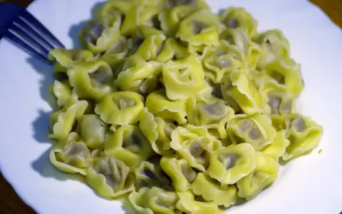Talerz pełen ugotowanego tortellini z widelcem po lewej stronie.
