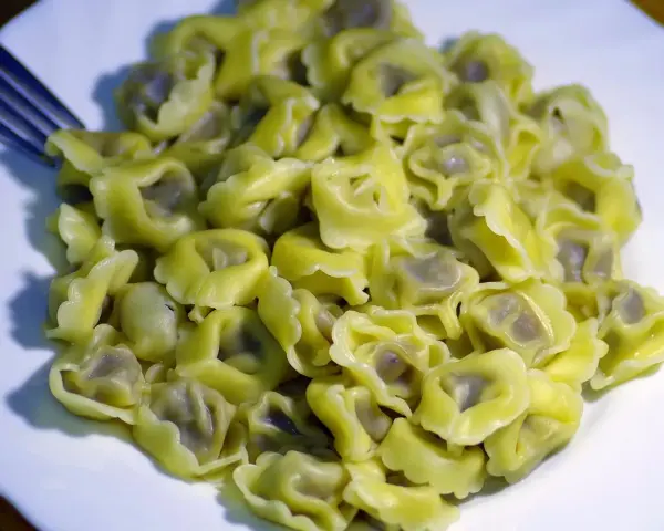Talerz pełen ugotowanego tortellini z widelcem po lewej stronie.