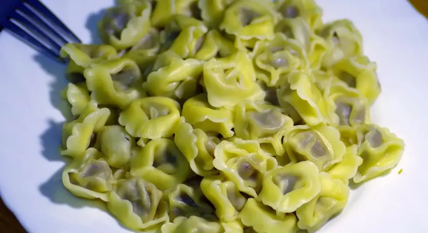 Talerz pełen ugotowanego tortellini z widelcem po lewej stronie.