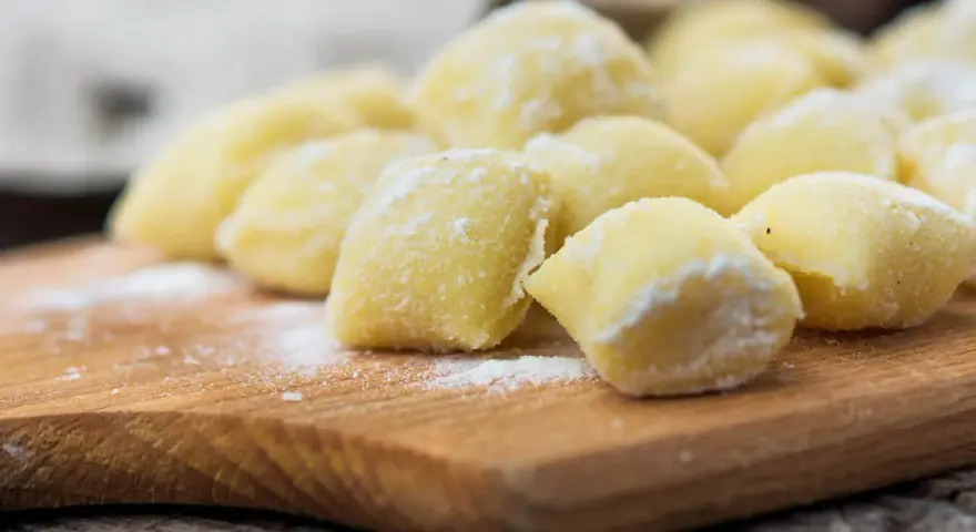 Mrożone kluski śląskie na drewnianej desce, posypane mąką.