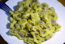 Talerz pełen ugotowanego tortellini z widelcem po lewej stronie.